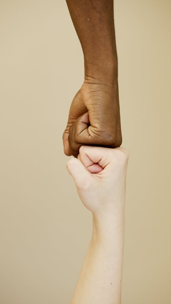 KollegialeZEIT Close-up of two diverse hands in a fist bump on a beige background, symbolizing unity.